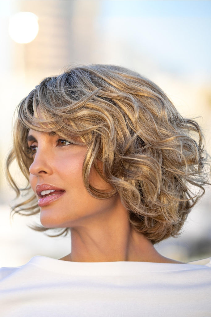 Women modeling a loose waved wig with fringe in softer dark blonde with light golden blonde and chestnut roots.