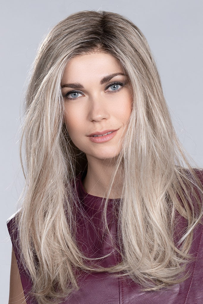 Close up of model smiling as she is wearing a wig in  the color Pearl Blonde Rooted.