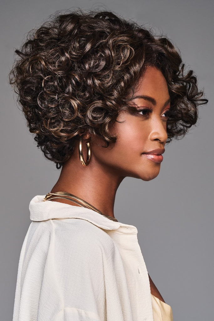 Side of women wearing a short voluminous bob style wig with sprial curls and layers.