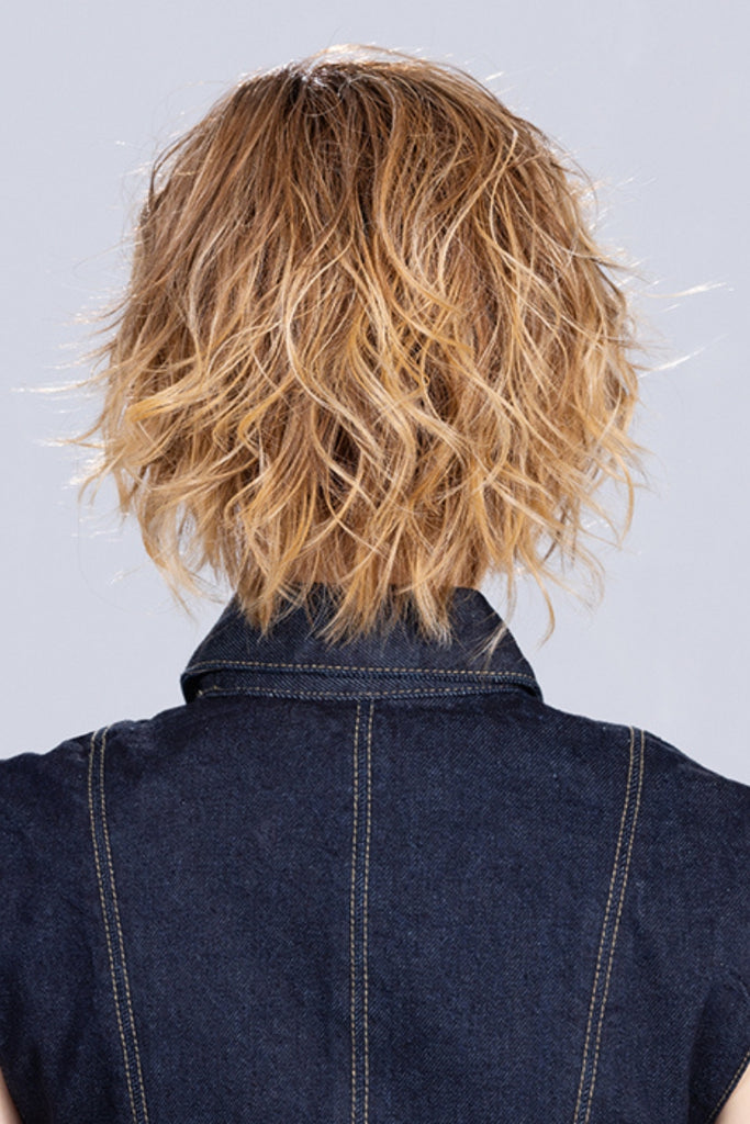 Woman wearing a curly bob style in a caramel blonde color with dark rooting.