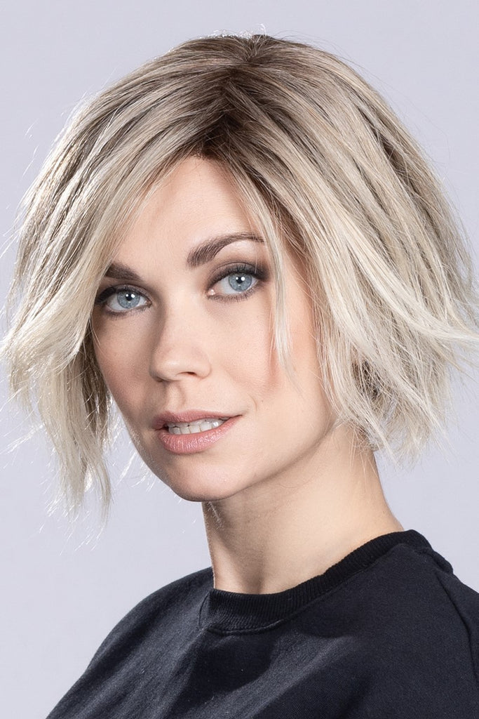 Model wearing a wig in a light beige blonde and pale blonde blend with dark roots.