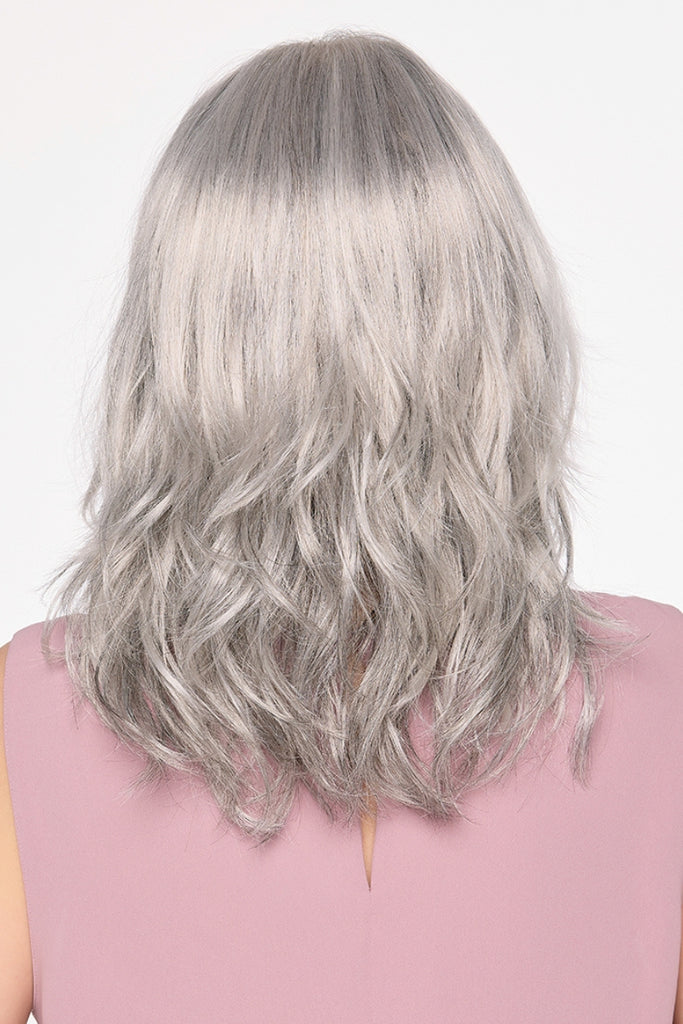 Back of model styling a shoulder-length, wavy wig in the color Medium Grey.