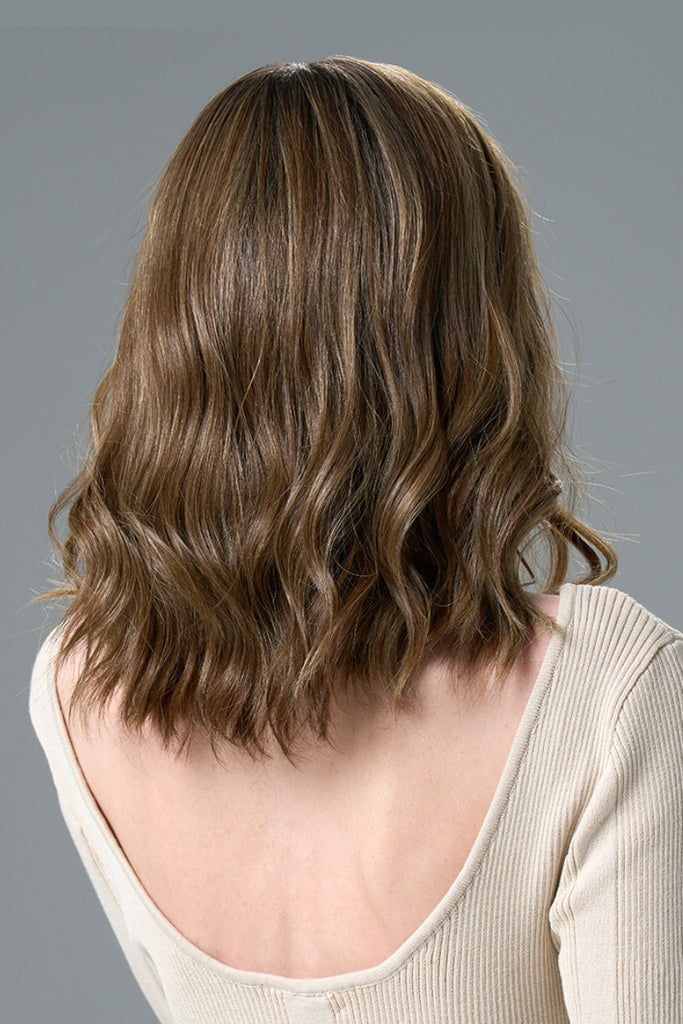 Woman wearing a wavy wig in a light brunette, honey blonde blend.