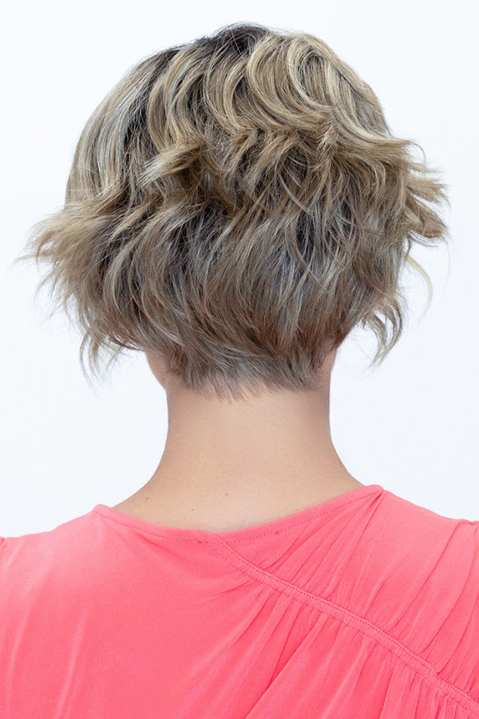 Back of model styling a wavy shag wig in the color Golden Sandstone.