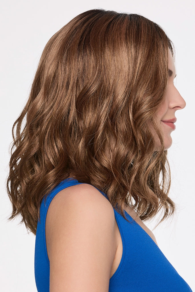 Side view of woman wearing a mid-length, wavy wig in a dimensional, light auburn color.