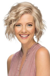 Smiling woman showing of a chic wavy wig, Wynter by Estetica in a natural blonde.
