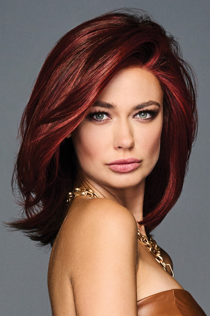 Confident women looking into the camera as she wears a deep ruby red wig with face framing layers.